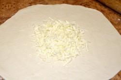 Рецепт - ХАЧАПУРИ ПО-МЕГРЕЛЬСКИ - Шаг 8 -  На этом этапе включите духовку на разогрев (за 10-15 минут до выпекания). Выставите температуру 190 градусов. Так как духовки у каждого пекут по-разному, учтите это. Возможно вам понадобится изменить температуру и время выпекания. Подробнее читайте в статье, ссылку на которую найдете в конце рецепта. На серединку круглой лепешки выложите 2/3 натертого сыра.